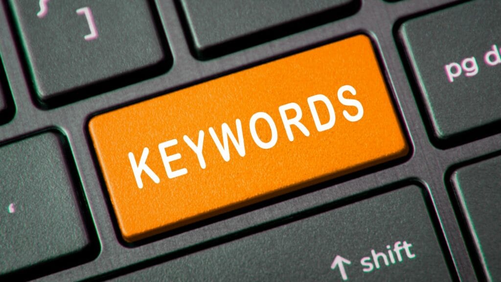 Close-up of a computer keyboard with a prominent orange key that has the word 'KEYWORDS' printed on it in white.